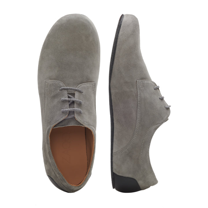 Der ZAQQ IQON Velours Grey präsentiert sich in einem schlichten Design mit runder Spitze, Schnürsenkeln und hellbraunem Innenfutter. Diese Business-Barfußschuhe sind sowohl von oben als auch von der Seite zu sehen. Die dünne Kautschuksohle bildet einen scharfen Kontrast zur weichen Textur des Wildleders und verleiht dem Schuh einen eleganten Touch.