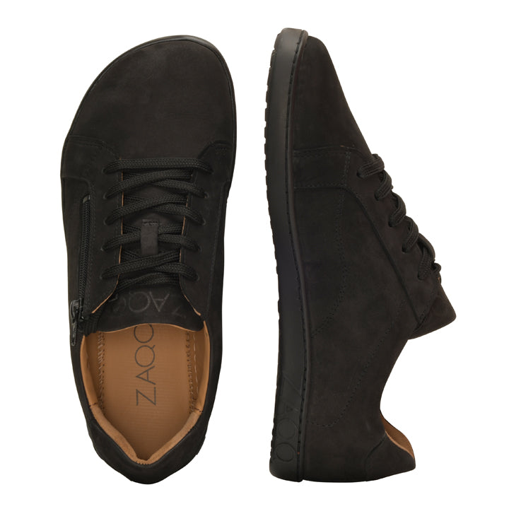 Die ZAQQ QOMFY Wide Black Sneaker werden in einer Seiten- und Draufsicht gezeigt und zeigen ihr einzigartiges Design, wobei ein Schuh einen Schnürverschluss und der andere einen Reißverschluss hat. Sie ruhen auf einer strukturierten SNEAKER-Sohle, verfügen über ein hellbraunes Innenfutter und ein elegantes Veloursleder-Finish.