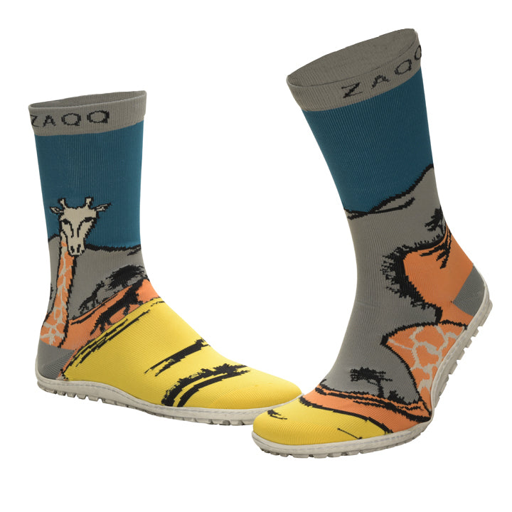 Die SOQQ Giraffe Yellow-Socken von ZAQQ zeigen mit ihrem lebendigen Design einen einzigartigen und künstlerischen Stil. Diese farbenfrohen Socken zeigen ein Giraffenmotiv vor einem felsigen Hintergrund in den Farbtönen Blau, Orange und Giraffengelb. Sie sind aus Strickgewebe gefertigt und der Markenname ist oben auf den Socken deutlich zu sehen.