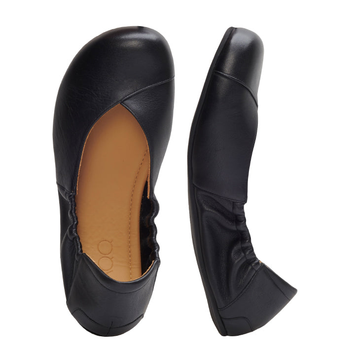 Ein Paar schwarze MAIQA Ballerinas von ZAQQ von oben betrachtet. Ein Schuh liegt flach und zeigt eine hellbraune Innensohle, während der andere auf der Seite liegt und einen elastischen Absatz hervorhebt – ideal für die modebewusste Frau.