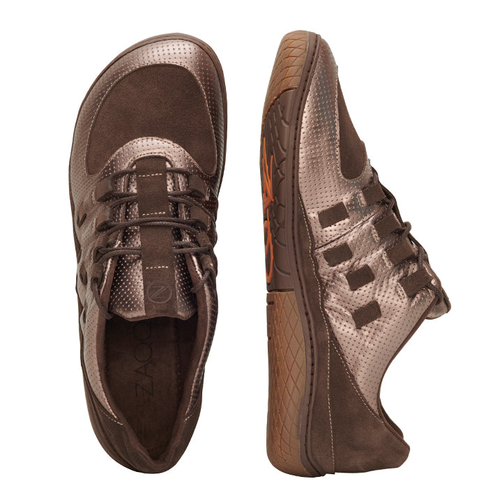 Wir präsentieren die BRISQ Bronze-Sneaker von ZAQQ: Ein elegantes Paar brauner Sneaker mit BRISQ Bronze-Akzenten und perforiertem Leder sowie Wildlederdetails. Der linke Schuh ist von oben zu sehen, während der rechte eine gemusterte Sohle aufweist, die eine minimalistische Sohle-Designästhetik widerspiegelt.