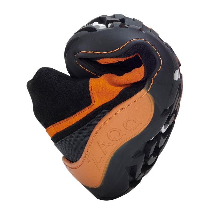 Ein schwarz-orangefarbener ZAQQ SQOUT Black Orange Waterproof Barfußschuh wird in aufgerollter Position präsentiert, um seine Flexibilität zu demonstrieren. Er verfügt über ein robustes Profil auf der Sohle, das ideal für abenteuerliches Gelände ist.