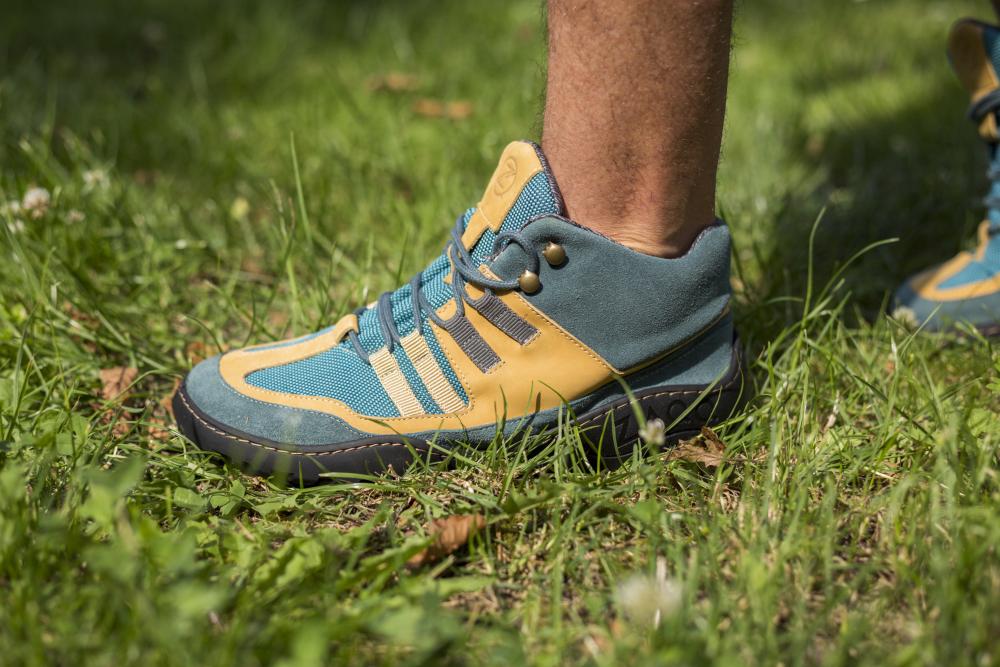 Eine Person, die die wasserdichten Wanderschuhe ESQAPE Blue Orange von ZAQQ mit TERRA-Sohle trägt, steht auf einer Wiese.