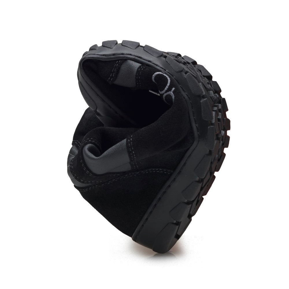 Der HIQE Black Waterproof Schuh von ZAQQ hat eine dicke, strukturierte Sohle und ist in der Mitte gefaltet, um seine Flexibilität hervorzuheben. Der schwarze Barfuß-Outdoorschuh hat weiße Nähte am oberen Teil und bietet einen rutschfesten Halt, wodurch er sich ideal für jedes Abenteuer eignet.