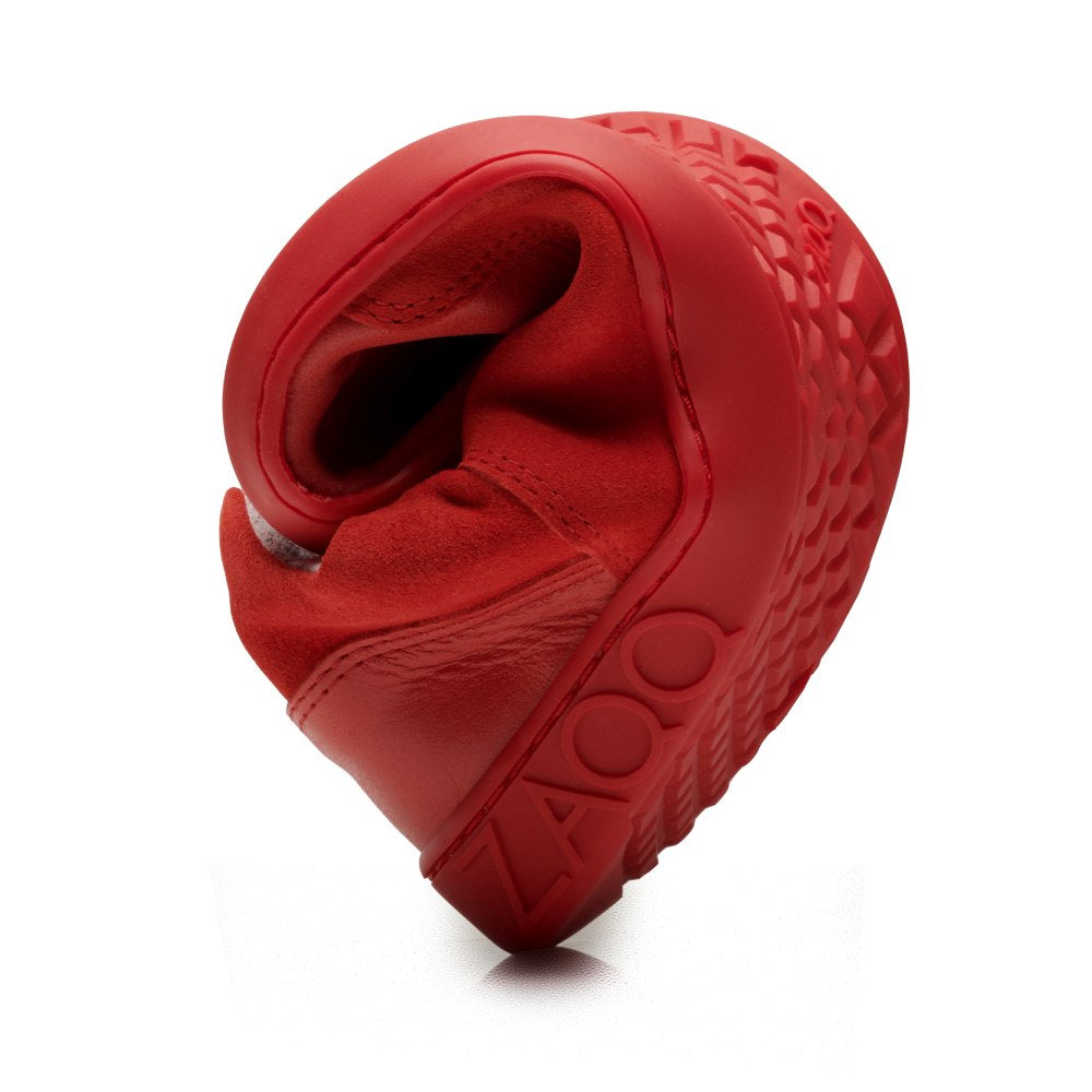 Ein leuchtender Sneaker in IVIQ Red von ZAQQ ist in eine kompakte Spiralform gerollt und zeigt so seine Flexibilität. Das Barfußschuh-Design umfasst eine strukturierte Sohle mit dem eingeprägten ZAQQ-Namen. Das Bild wird vor einem einfachen weißen Hintergrund präsentiert.