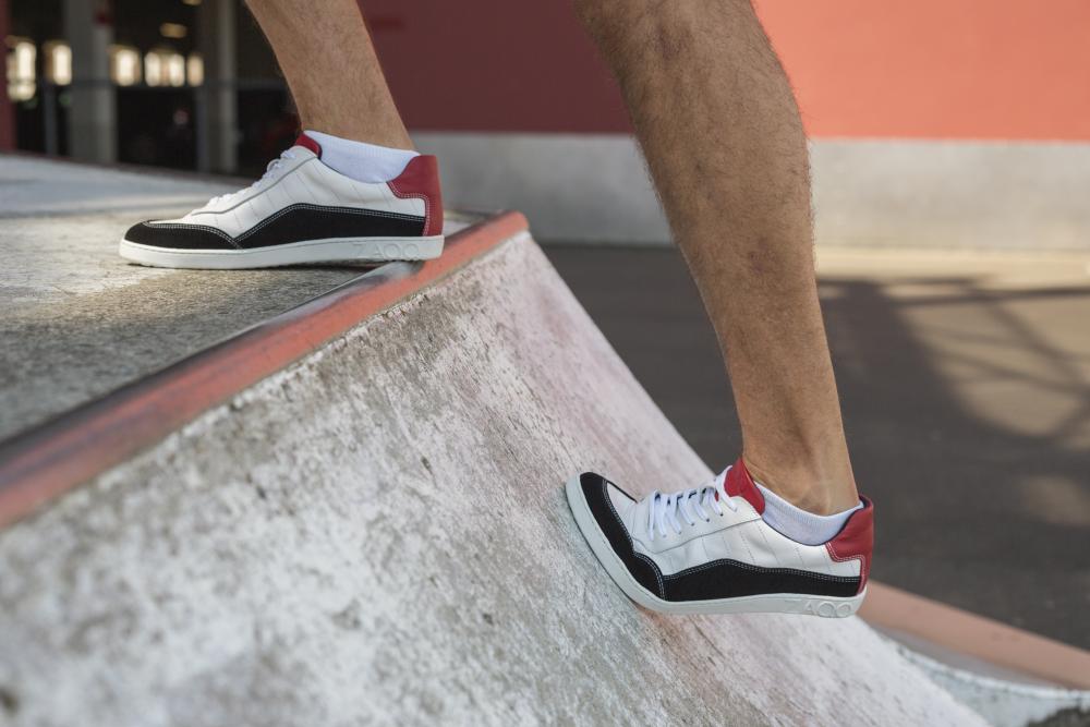 Nahaufnahme einer Person, die ZAQQs QAMPION Black White-Sneaker mit flexibler Sohle trägt und eine Betonrampe in einem Skatepark hochsteigt. Im Hintergrund sind eine rote Wand und ein Teil einer Tür zu sehen.