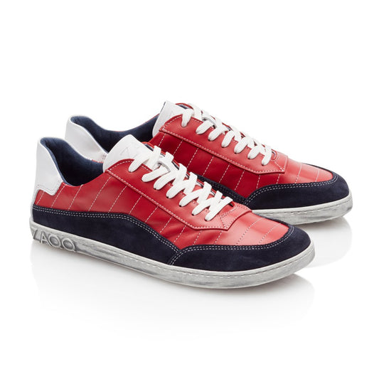 Wir präsentieren den QAMPION Navy Red von ZAQQ: ein Paar stylische Sneaker mit Obermaterial aus rotem Nappaleder, ergänzt durch marineblaue Wildlederakzente und weiße Schnürsenkel. Die Schuhe verfügen über ein elegantes weißes Logo an der Seite und ruhen auf einer grauen Sohle mit abgenutzter Textur, alles vor einem strahlend weißen Hintergrund.