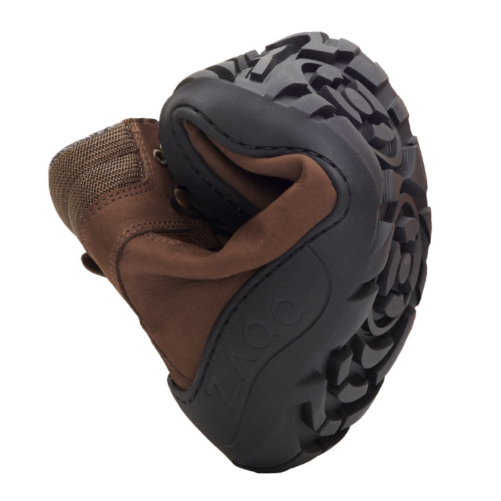 Ein brauner, wasserdichter Wanderschuh MOUNTEQ Brown von ZAQQ mit einer flexiblen, gebogenen Sohle, die ihr Profilmuster zur Schau stellt. Der Schuh verfügt über ein Obermaterial aus Mesh und Leder, ideal für alle, die bei Outdoor-Abenteuern den Komfort von Barfußschuhen suchen.