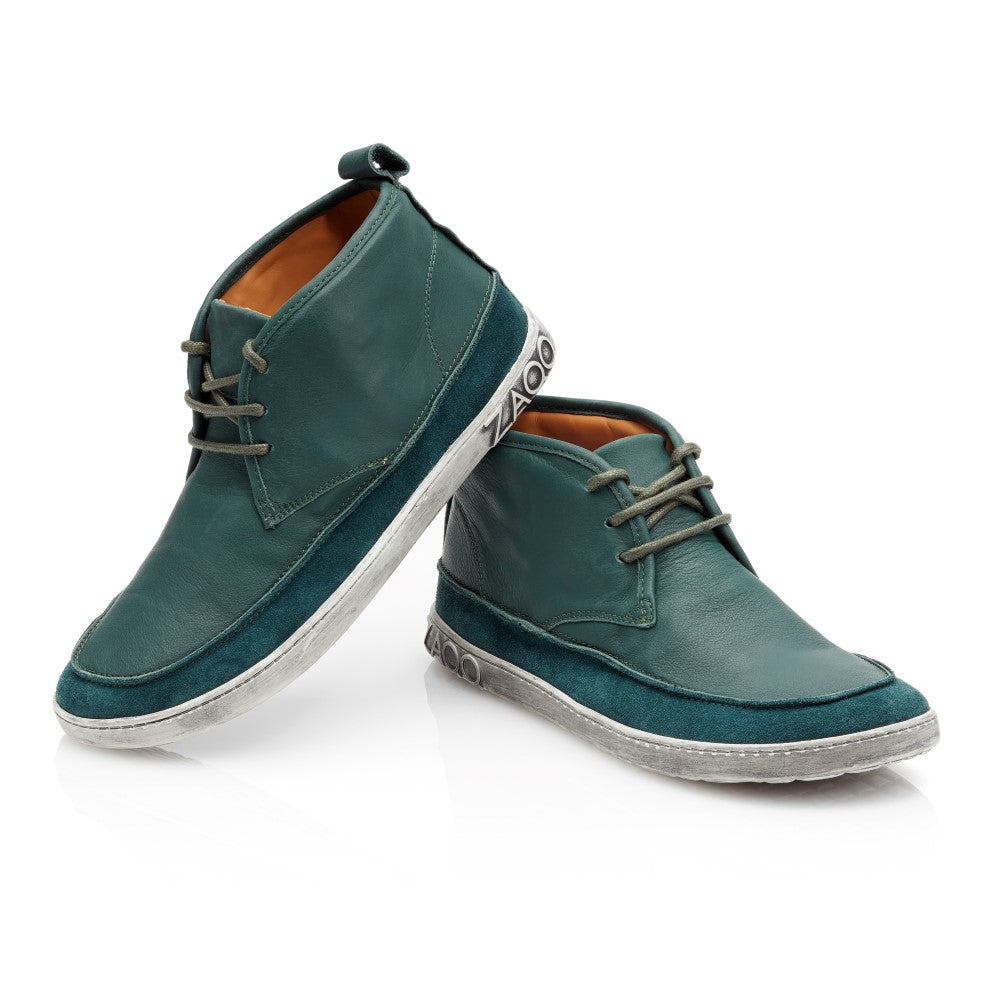 Wir präsentieren die QUITMAN Green Stiefeletten von ZAQQ, gefertigt aus einer Kombination aus Velours und Glattleder. Diese stylischen Schuhe haben graue Schnürsenkel und eine leicht abgenutzte weiße Gummisohle und verbinden das elegante Design von Sneakers mit einer bequemen Passform, wunderschön präsentiert auf einem weißen Hintergrund.