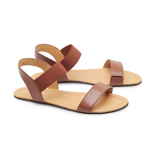 Ein Paar SLIQ Cognac-Sandalen von ZAQQ in Braun, mit breiten Riemen und einer flachen Kautschuksohle für maximalen Komfort. Die gepolsterte Innensohle bietet ein angenehmes Laufgefühl und die Sandalen sind elegant nebeneinander auf weißem Hintergrund ausgestellt, was ihr schlichtes, aber stilvolles Design unterstreicht.