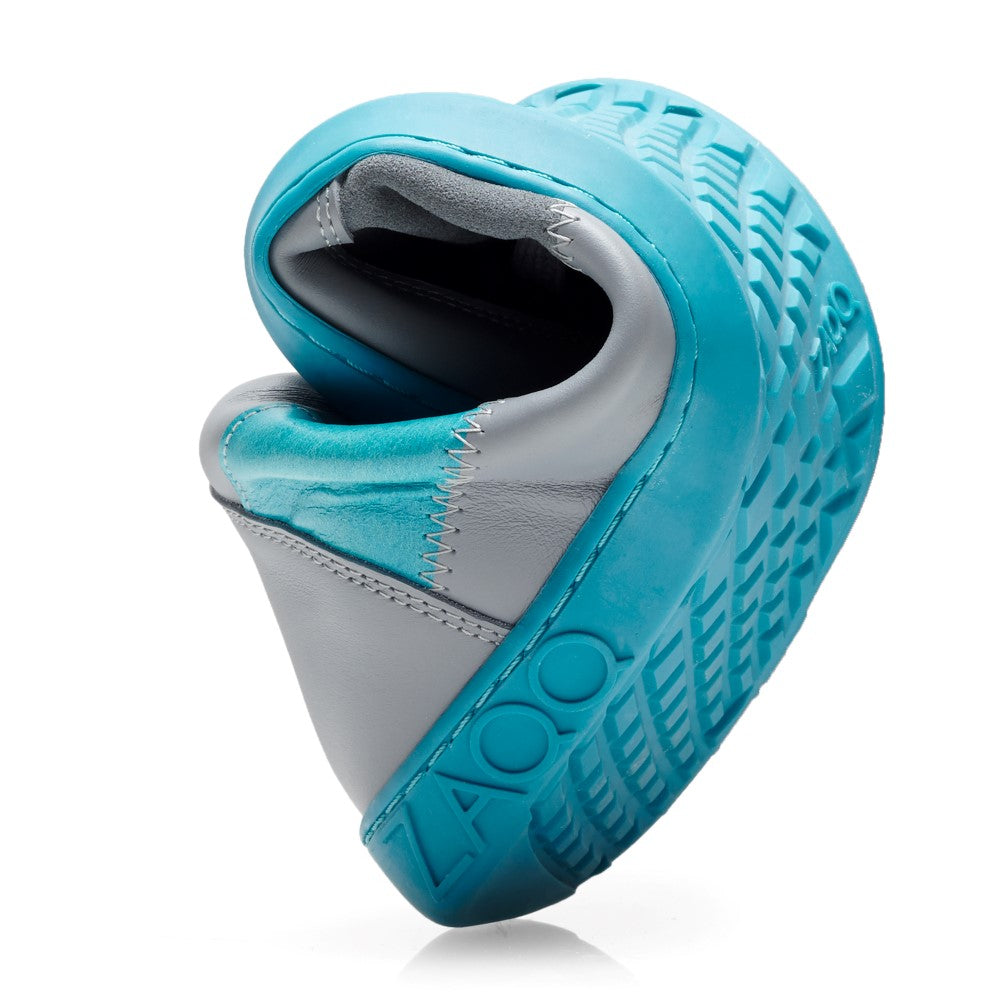 Der LUQQ Turquoise Sneaker von ZAQQ mit flexibler Gummisohle ist in der Mitte gebogen. Er zeigt ein blau-graues Farbschema mit strukturierten Mustern auf der Sohle und hat „LADO“ sichtbar. Die Nähte sind auf dem oberen Teil dieses stilvollen Schuhs deutlich zu sehen.