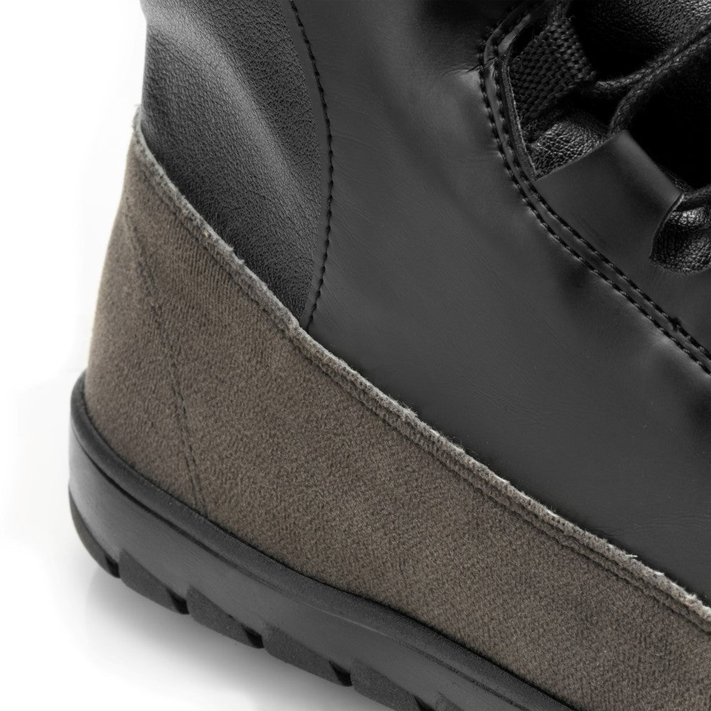 Eine Nahaufnahme des QUEST Black Waterproof-Stiefels von ZAQQ hebt seine aufwendigen Nähte und seine Textur hervor. Dieser Outdoorschuh ist aus einer Kombination aus glattem schwarzem Leder und grauem Wildleder gefertigt und verfügt über eine solide schwarze Gummisohle mit sichtbarem Profil. Sein wasserdichtes Design sorgt für ultimative Haltbarkeit unter unterschiedlichsten Bedingungen.