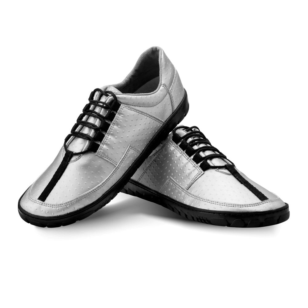 Ein elegantes Paar JAQ Silver Barfuß-Sneaker von ZAQQ mit schwarzer Sohle und Schnürung. Der rechte Schuh steht aufrecht, während der linke stilvoll auf der Seite vor einem weißen Hintergrund liegt und so das Design hervorhebt. Mit einer flexiblen Kautschuksohle sorgen diese Sneaker für höchsten Komfort und Flexibilität.