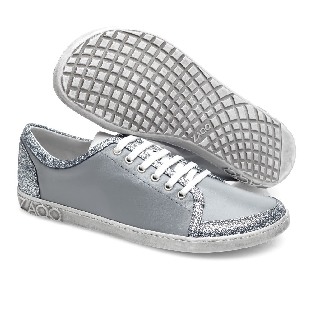 Wir präsentieren den TIQQ Grey Silver von ZAQQ: Diese stylischen Sneaker bestechen durch elegante Seitenteile aus hellgrauem Nappaleder gepaart mit funkelnden silbernen Akzenten an Ferse und Zehen. Die weißen Gummisohlen verfügen über ein strukturiertes Muster für besseren Halt und zeigen stolz das ZAQQ-Branding an der Seite und der Sohle. Dieses Paar verbindet mühelos Mode mit Funktionalität.