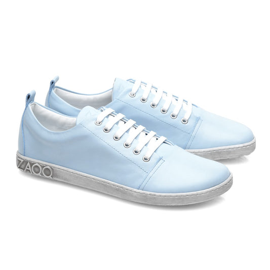 Die TAQQ Nappa Lightblue von ZAQQ sind ein stilvolles Paar hellblauer Schnürsneaker aus hochwertigem Nappaleder mit weißer Sohle und dem geprägten ZAQQ-Logo auf der Ferse. Diese Barfußschuhe sind kunstvoll diagonal vor einem weißen Hintergrund positioniert, um ihr schlichtes Design hervorzuheben.